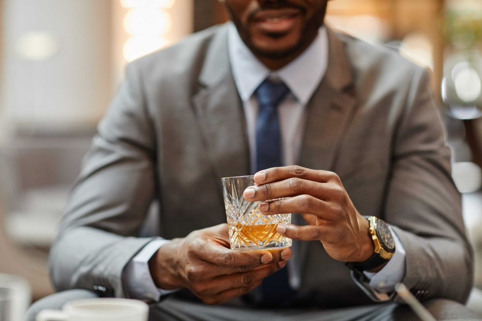 Cropped shot of successful African-American businessman enjoying glass of whiskey in hotel,