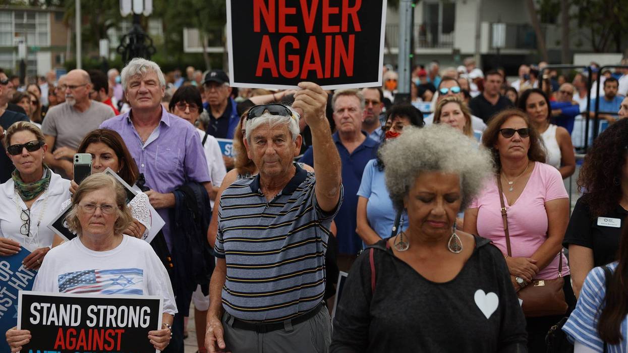 crowd of people, one man holds sign that says 'never again'