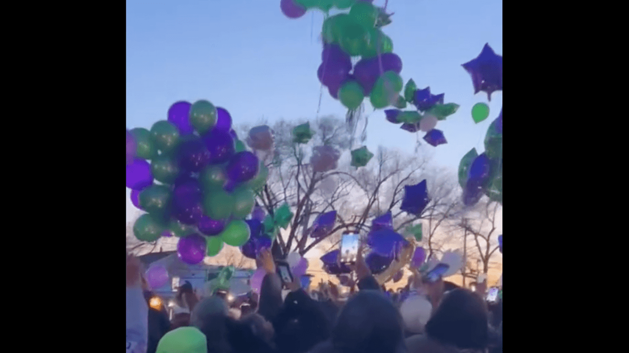 Crowd releasing green and purple balloons