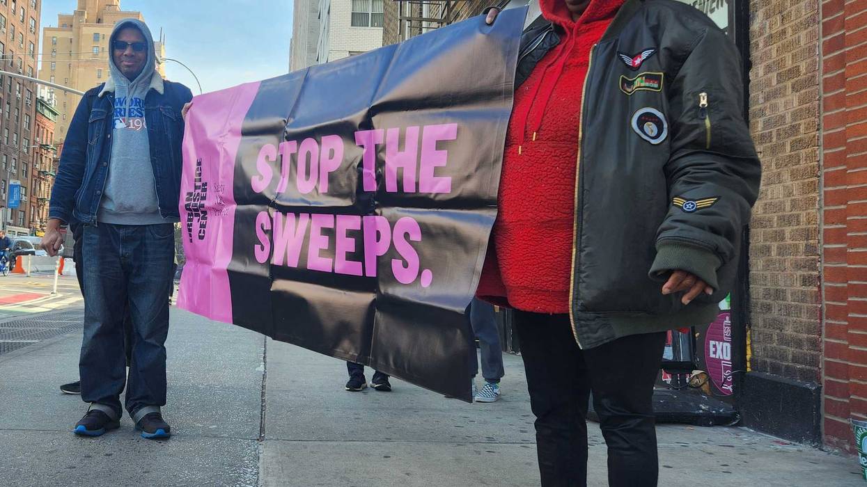 Crystal Vails (right) and a worker for the Urban Justice Center's Safety Net Project (left) hold a sign reading "stop the sweeps" as NYPD officers, sanitation workers and Department of Homeless Services workers approach to force Vails to move her belongings.