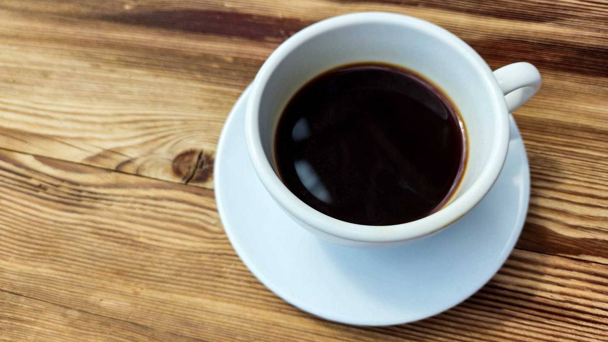 Cup of black coffee without milk in round white cup on brown wooden table background