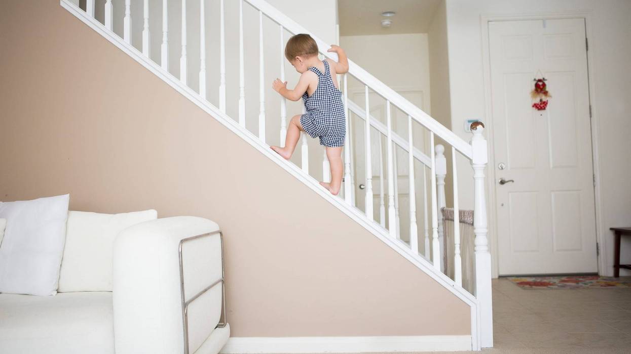 Cute toddler boy is climbing the stairways at home