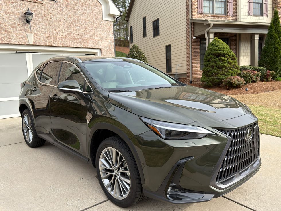 Dark green Lexus NX crossover parked on a driveway in front of a house.