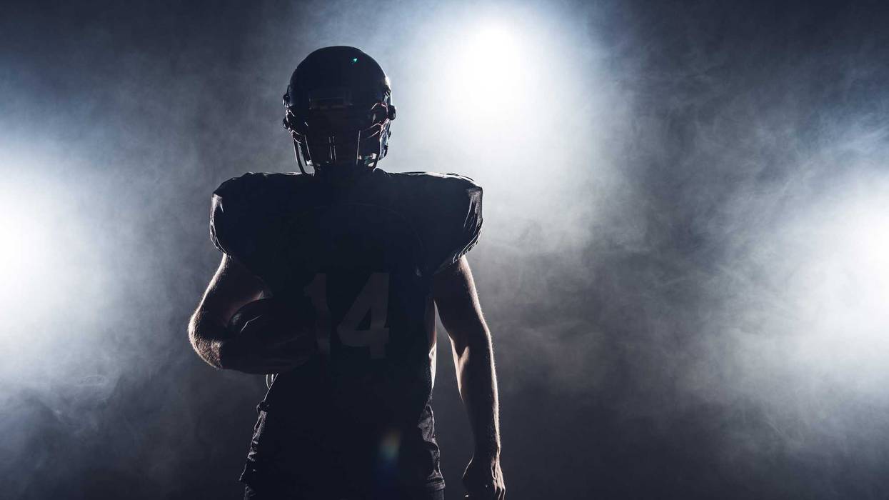 dark silhouette of football player with ball against white smoke