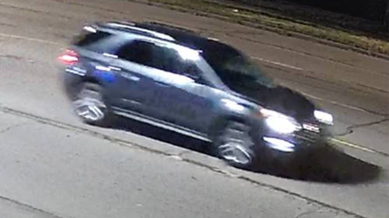 Dark SUV driving on a road at night with lights on. Features motion blur.