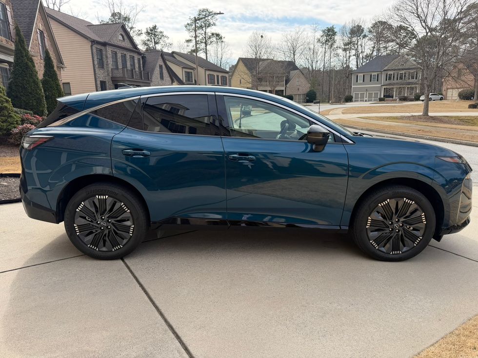 Dark teal SUV with black wheels and white accents, parked on a driveway in a suburban setting.