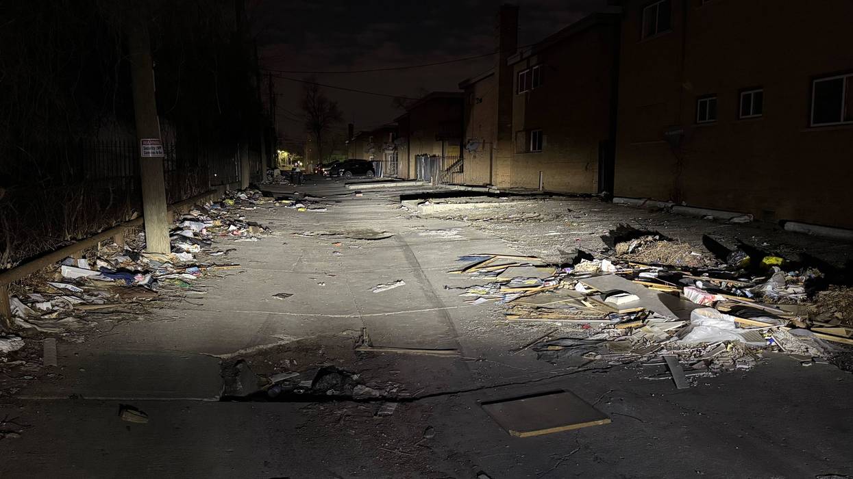 Dark urban alley at night, heavily littered with trash and debris.