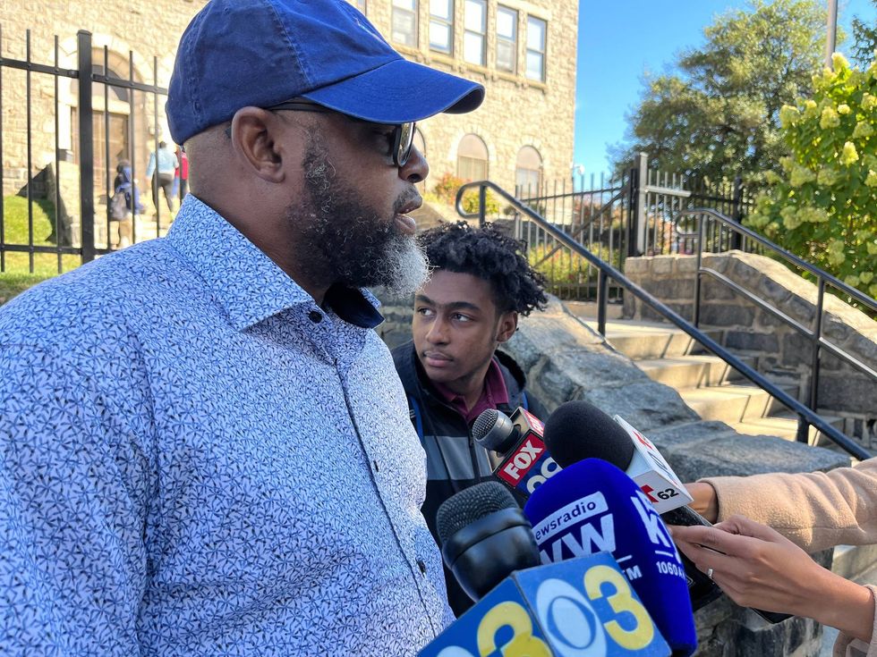 Darryl Johnson (left) speaks to reporters outside of Boys Latin Charter High School, where his son Taliq (right), is a senior.