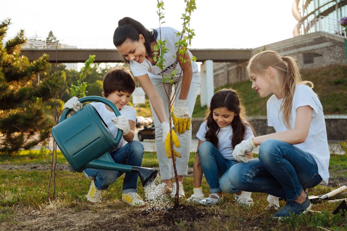 Delighted girls sitting around young tree and keeping smile on faces while looking at the process