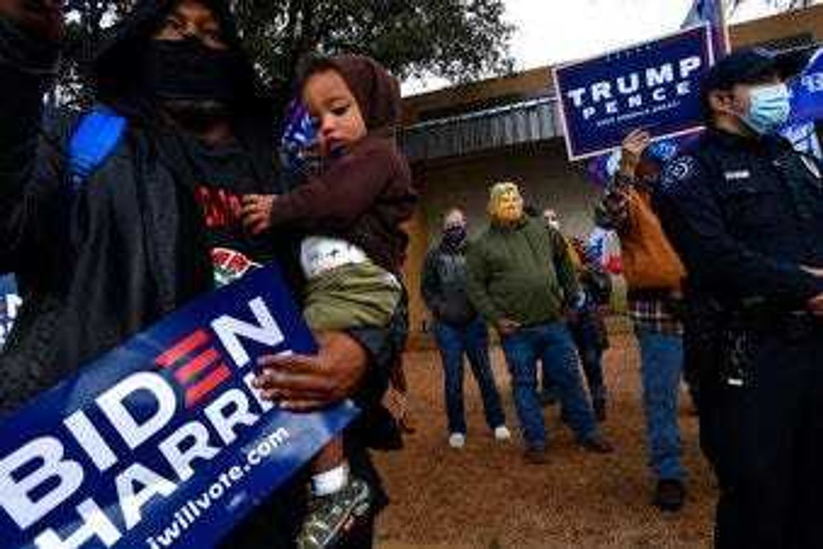 Demetrius Earthly balances his one-year-old son Brodrick and a Biden-Harris campaign sign, Wednesday, Oct. 28, 2020. Behind him, Toby Lindley wears a Donald Trump mask. (Ronald W. Erdrich/The Abilene Reporter-News via AP)
