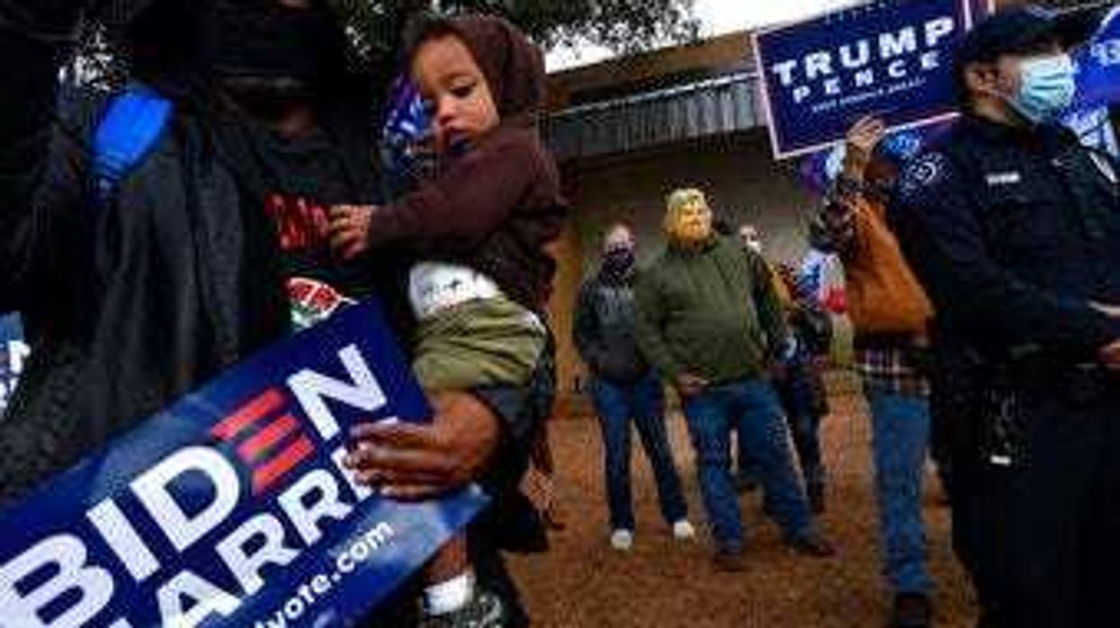 Demetrius Earthly balances his one-year-old son Brodrick and a Biden-Harris campaign sign, Wednesday, Oct. 28, 2020. Behind him, Toby Lindley wears a Donald Trump mask. (Ronald W. Erdrich/The Abilene Reporter-News via AP)