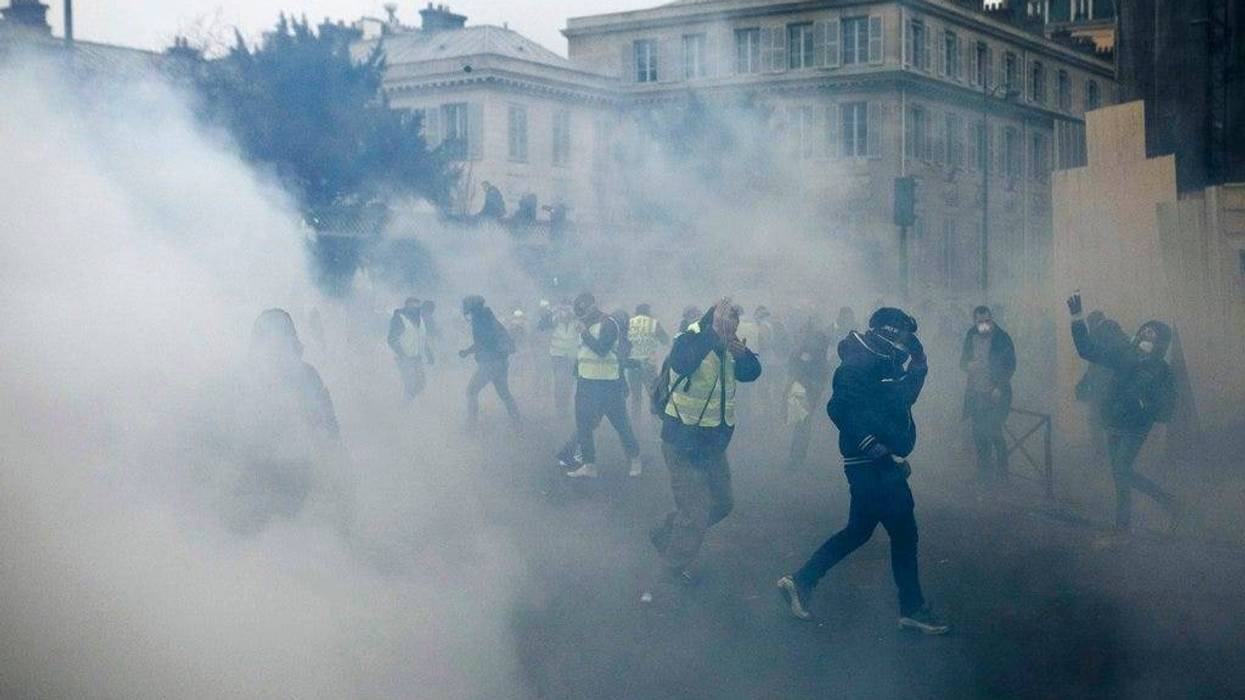 Demonstrators run as tear gas is thrown by riot police during a protest in Paris, Saturday, Jan. 5, 2019. Hundreds of protesters were trying to breathe new life into France's apparently waning yellow vest movement with marches in Paris and gatherings in o