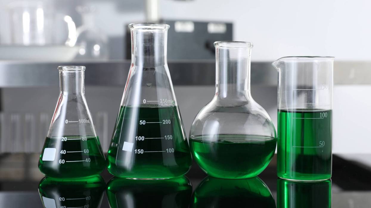 Different glassware with green liquid on table in laboratory, closeup