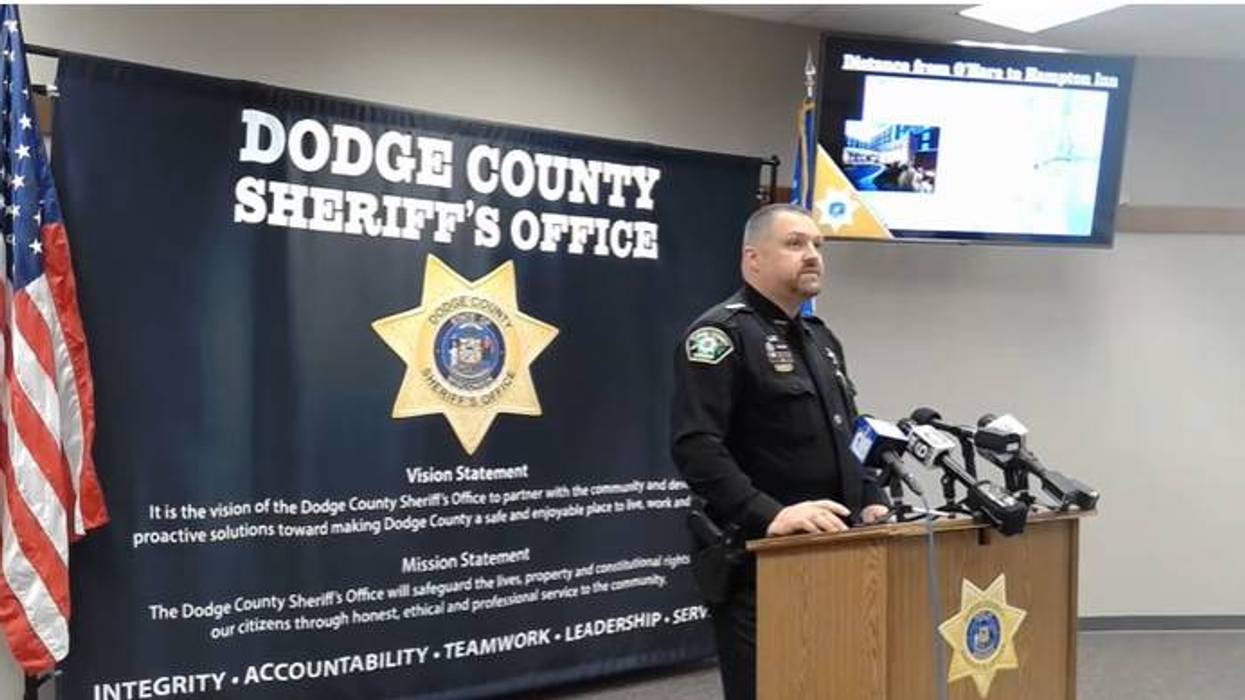 Dodge County Sheriff's officer speaks at a press conference, with office banner & US flag.
