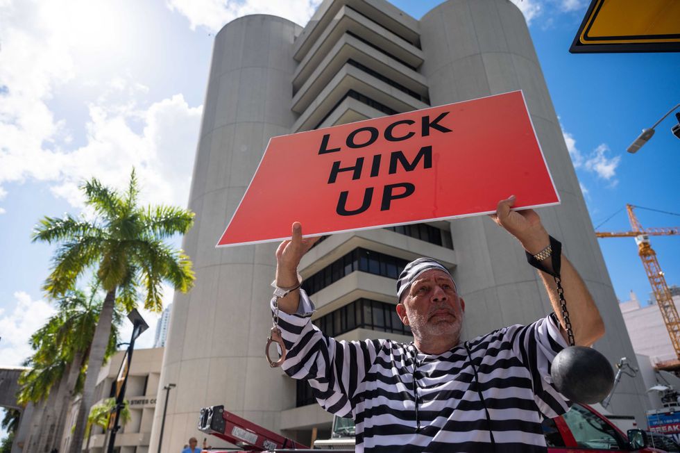 Dominic Santana, Miami, holds a sign reading "Lock him up" while wearing a striped prisoner