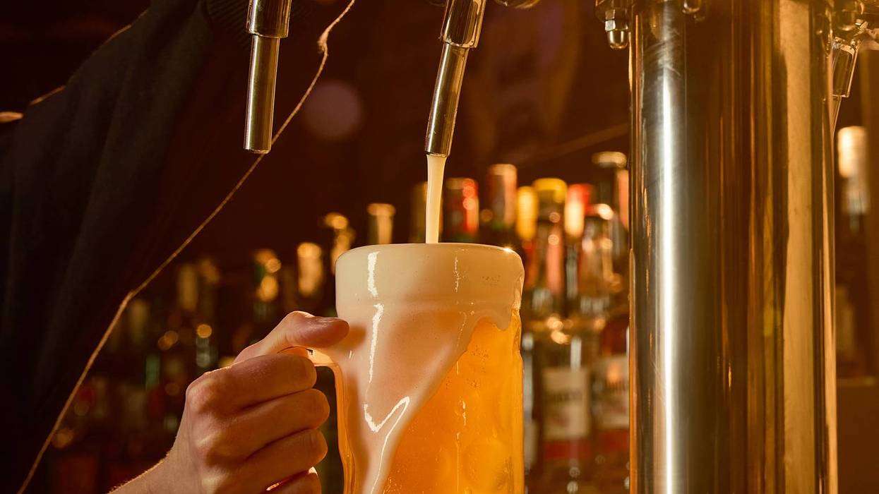 Draft beer pouring into glass mug with foam overflowing in warm bar lighting.