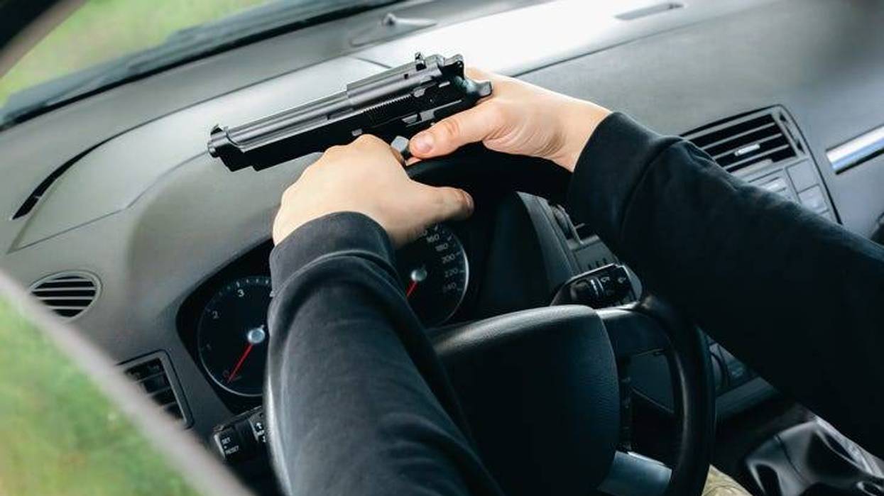 Driver's hands gripping the wheel. He holds a gun in his right hand.