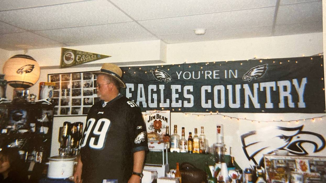 Eagles Fan Joe Flatley standing in front of a table in his "Eagles Nest" man cave and banner that reads: "You're in Eagles Country."