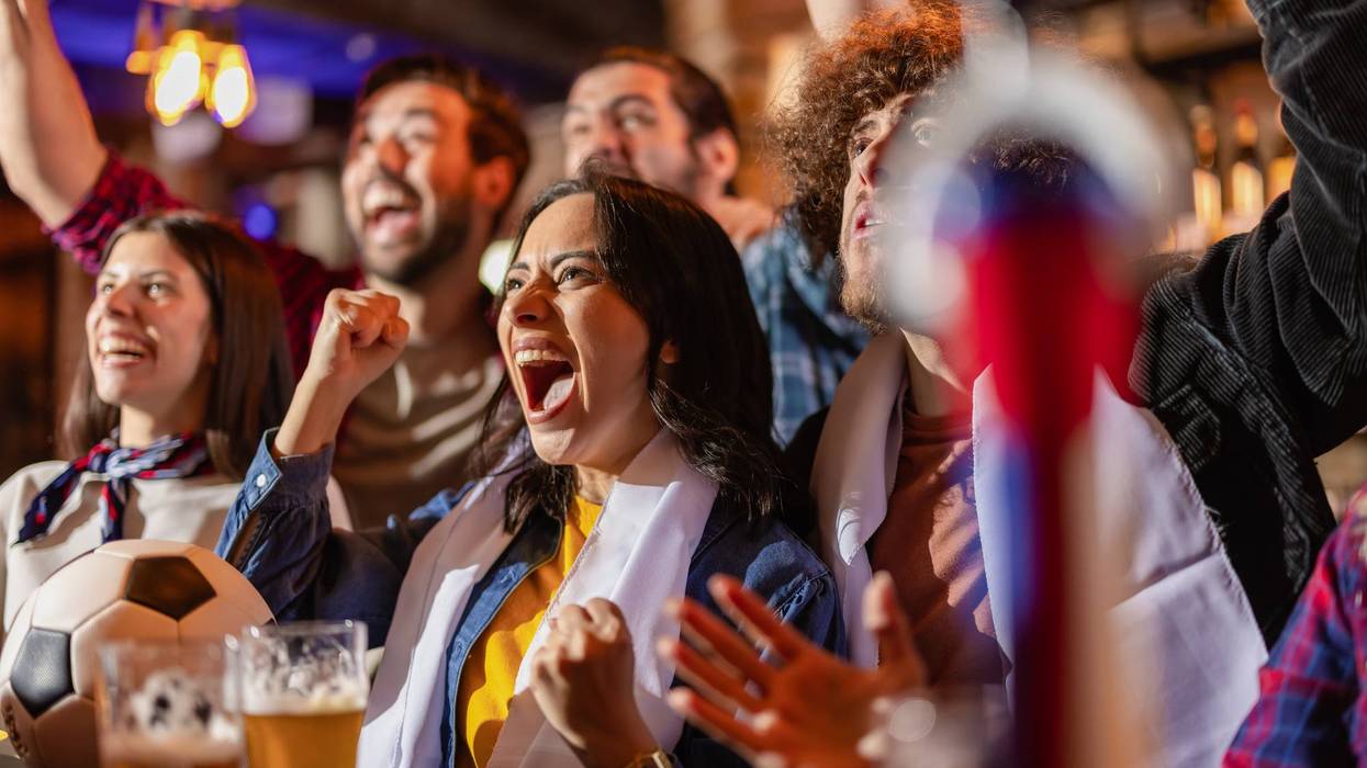 Ecstatic friends shouting and celebrating a soccer goal victory at a pub bar.