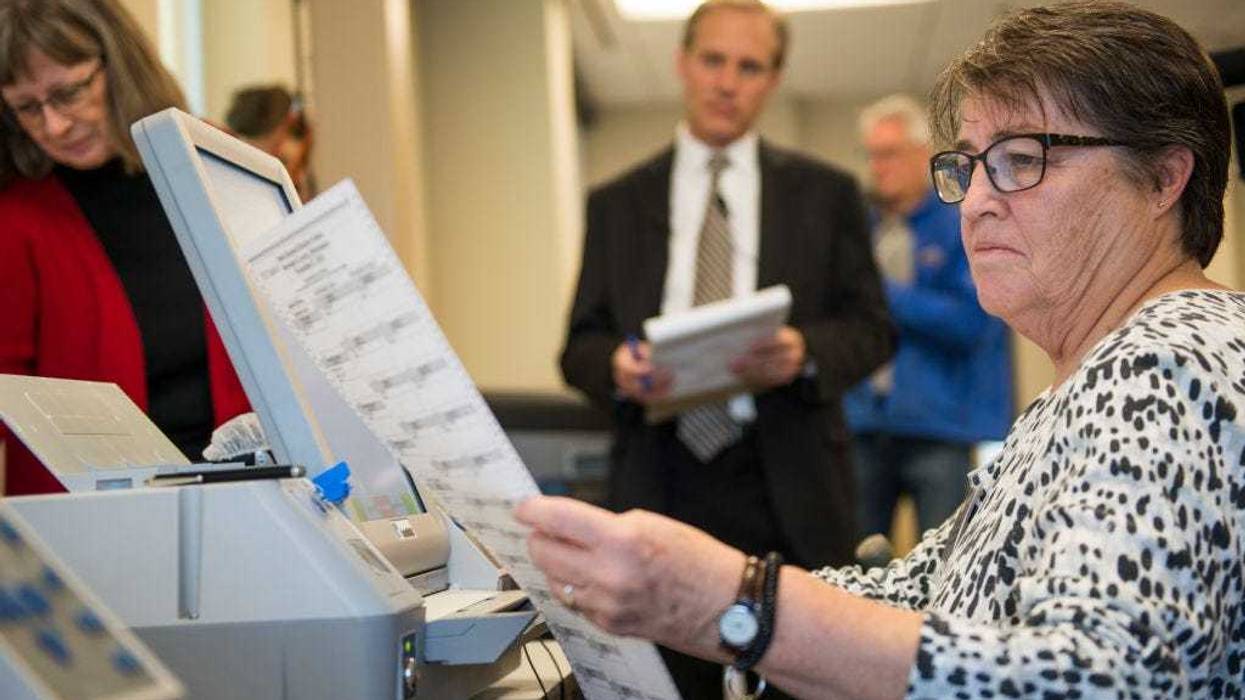 Election official Mary Wickersham (L) and Minnesota Secretary of State Steve Simon (C) look on as election official Mary Maynard enters selections into a voting machine during a public accuracy testing of Election Day voting machines.