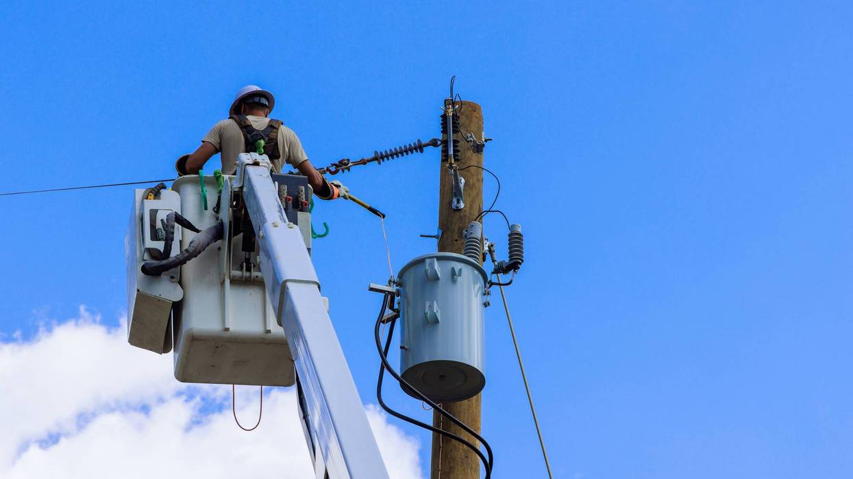 Electrician performs maintenance work on power line in clear blue sky at midday