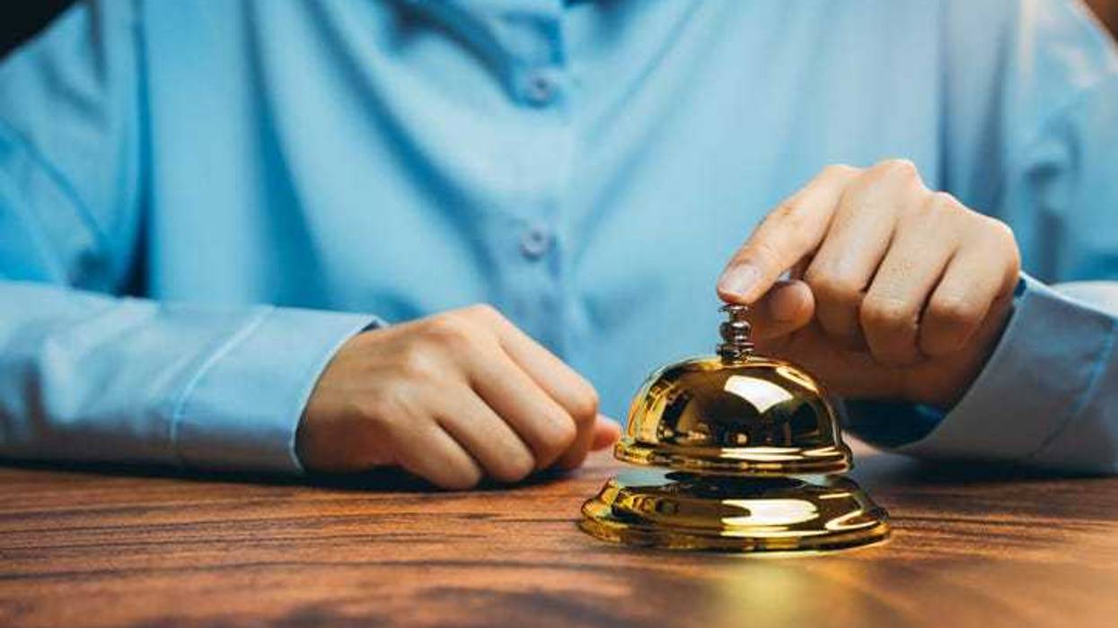 Elegant Gold Service Bell on Wooden Counter, Customer Interacting with Receptionist in Hospitality Setting