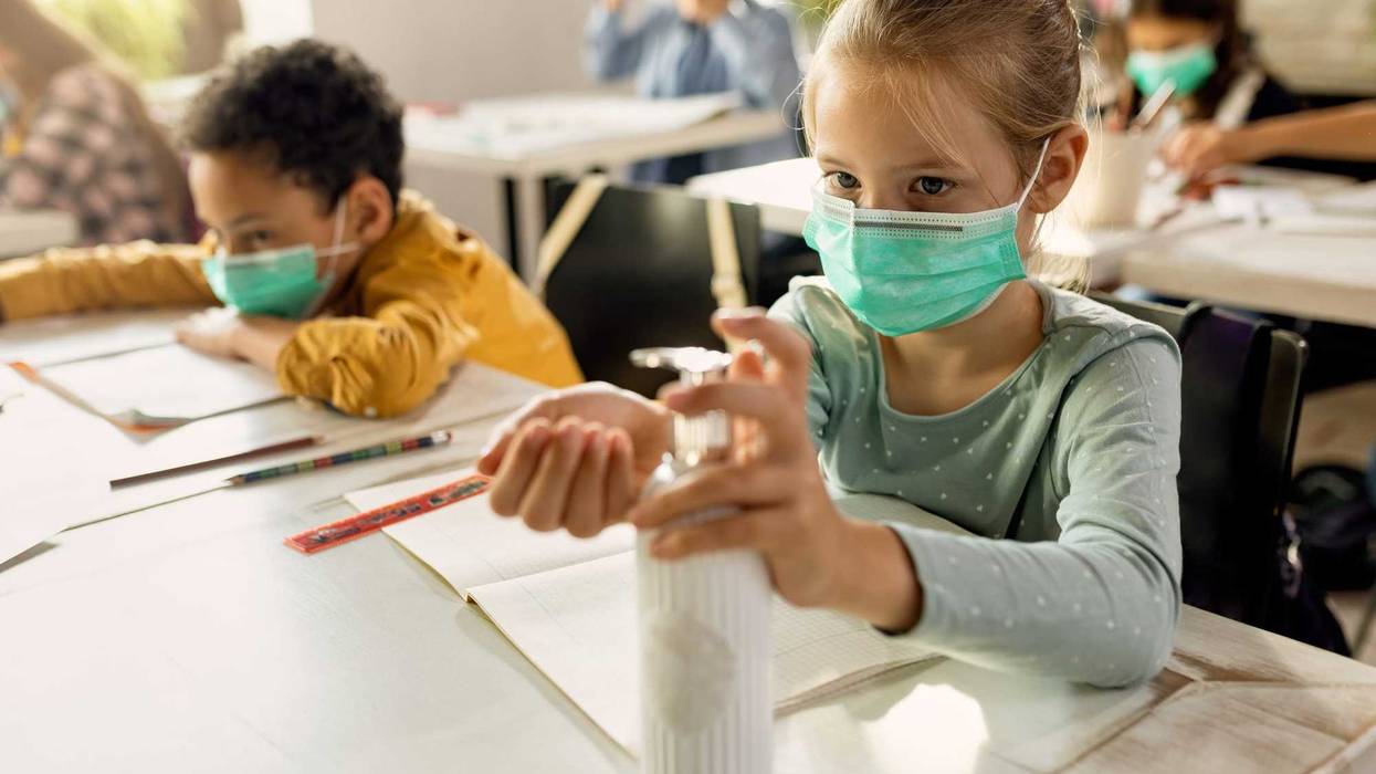 Elementary student wearing protective face mask and disinfecting her hands in the classroom