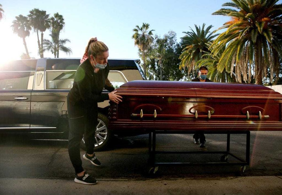 Embalmer and funeral director Kristy Oliver (L) and funeral attendant Sam Deras prepare to load the casket of a person who died after contracting COVID-19 into a hearse at East County Mortuary on January 15, 2021 in El Cajon, California.