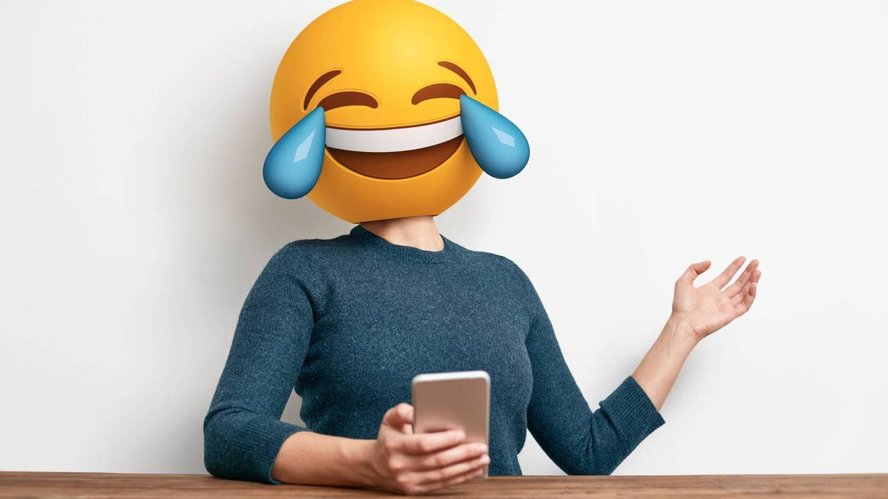 Emoji Head Woman sitting at desk. Woman wearing tears of joy emoji masks while looking at her phone. This emoji is laughing so much that it is crying tears of joy