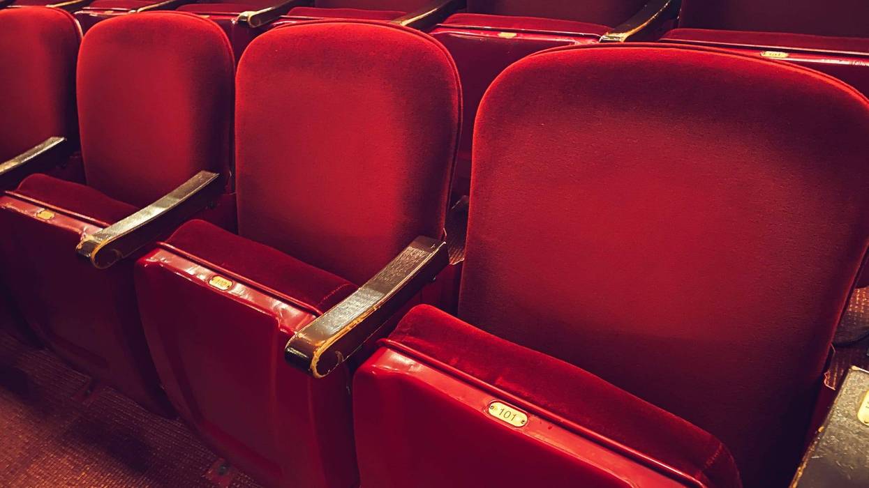 Empty cushioned red theater seats with gold numbers in movie theater cinema for viewing broadway show performances, movies and stage acting performances background