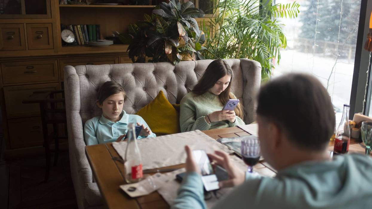 Family sitting at a table in a cafe, everyone looking at their smartphone. Children with their father waiting for their order in a restaurant, brother, sister and father surfing the Internet via mobil