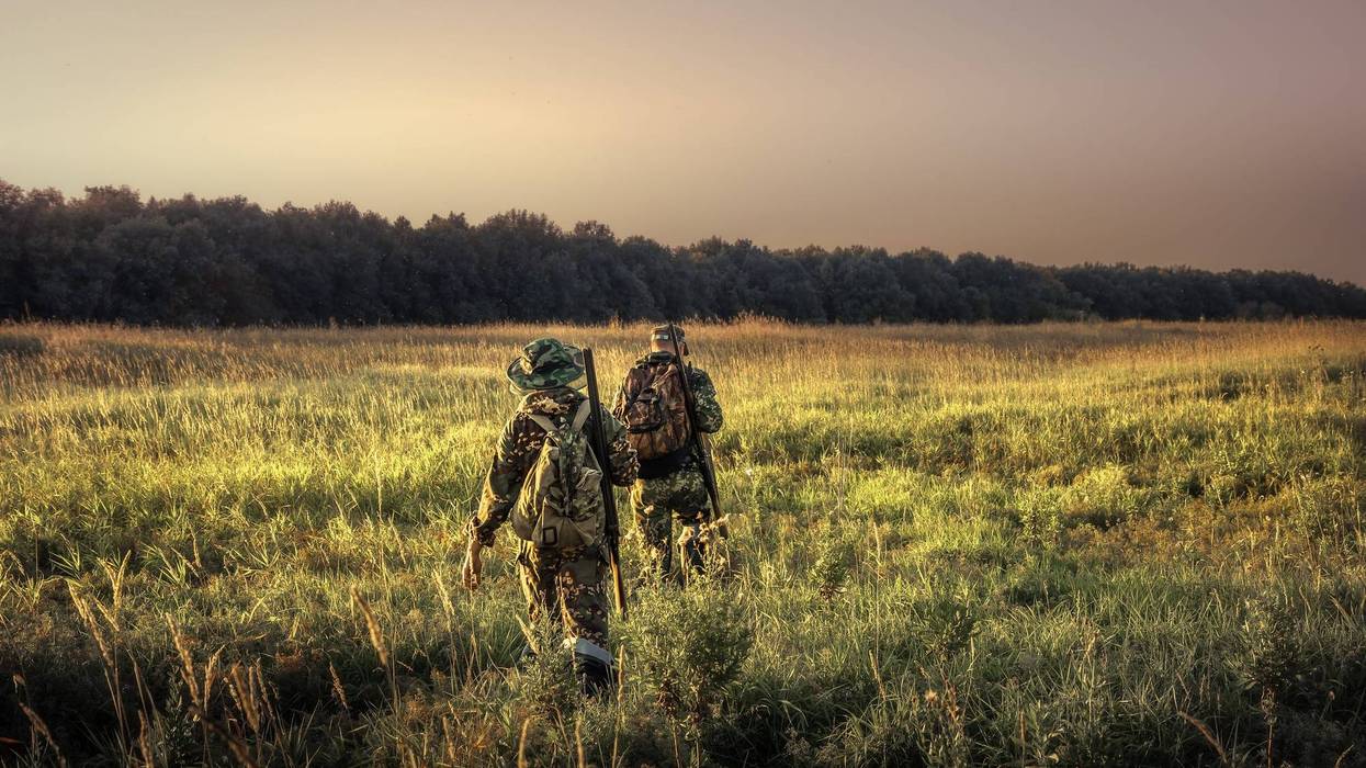 Father and son walking in field with hunting gear