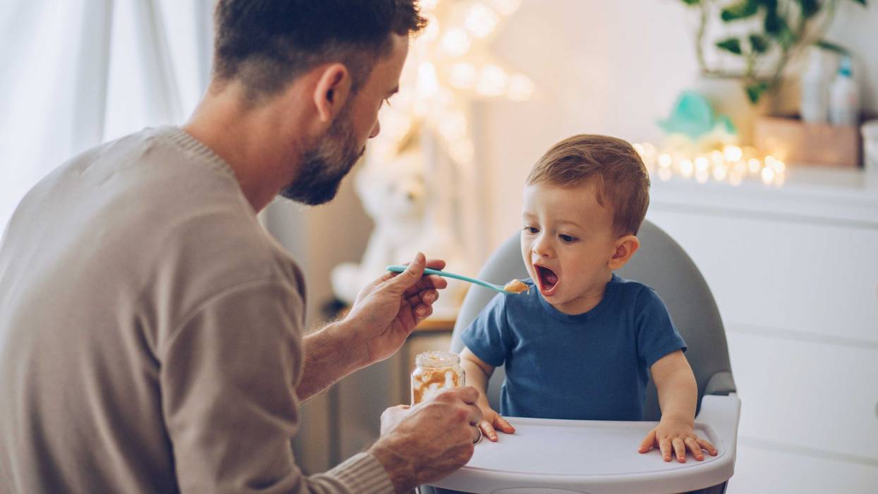 father feeding his little baby some baby food. baby's in a high chair