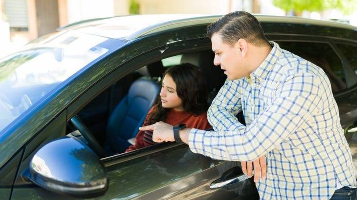 father instructing his teenage daughter on driving while pointing out something inside the car