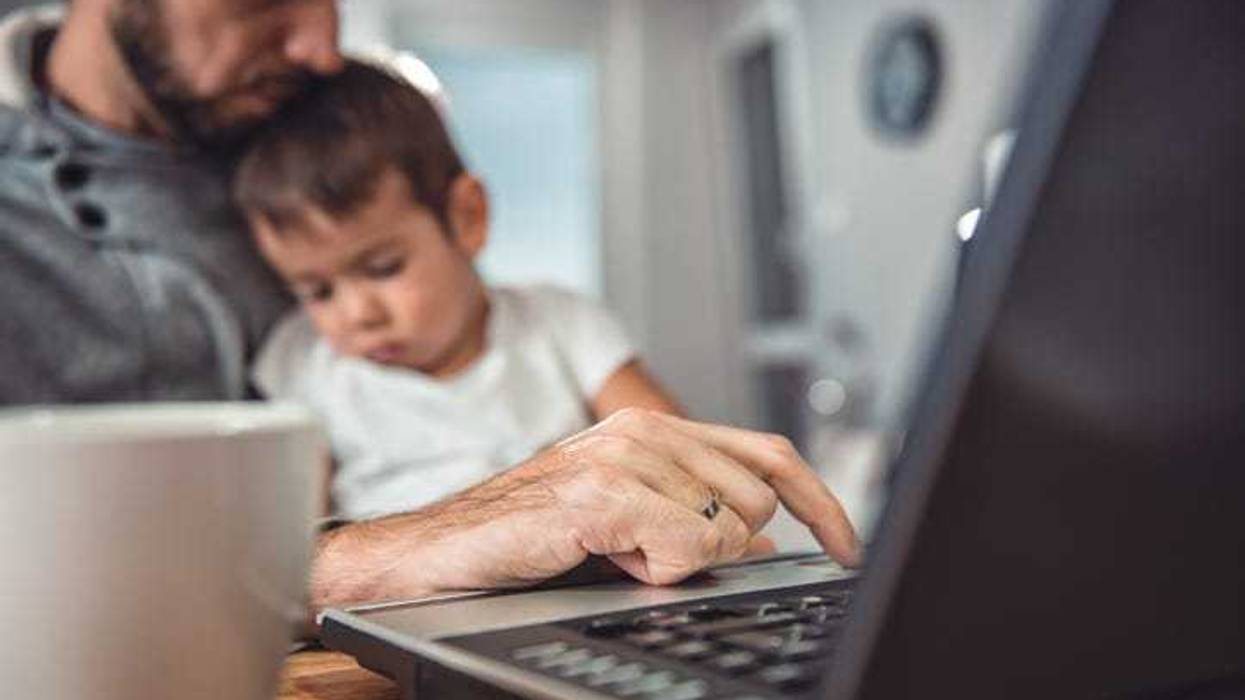 Father working on laptop at home office and holding son on his lap