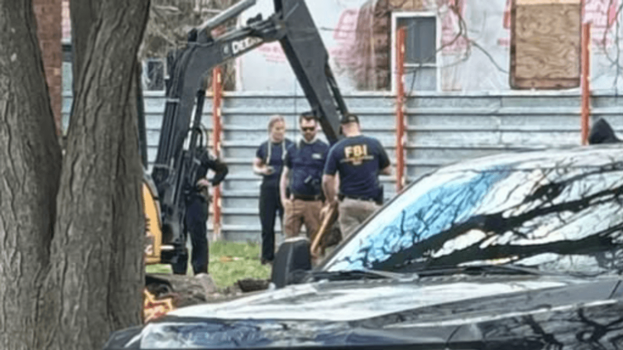 FBI agents and an excavator at a wrapped house, partly obscured by a black pickup truck.