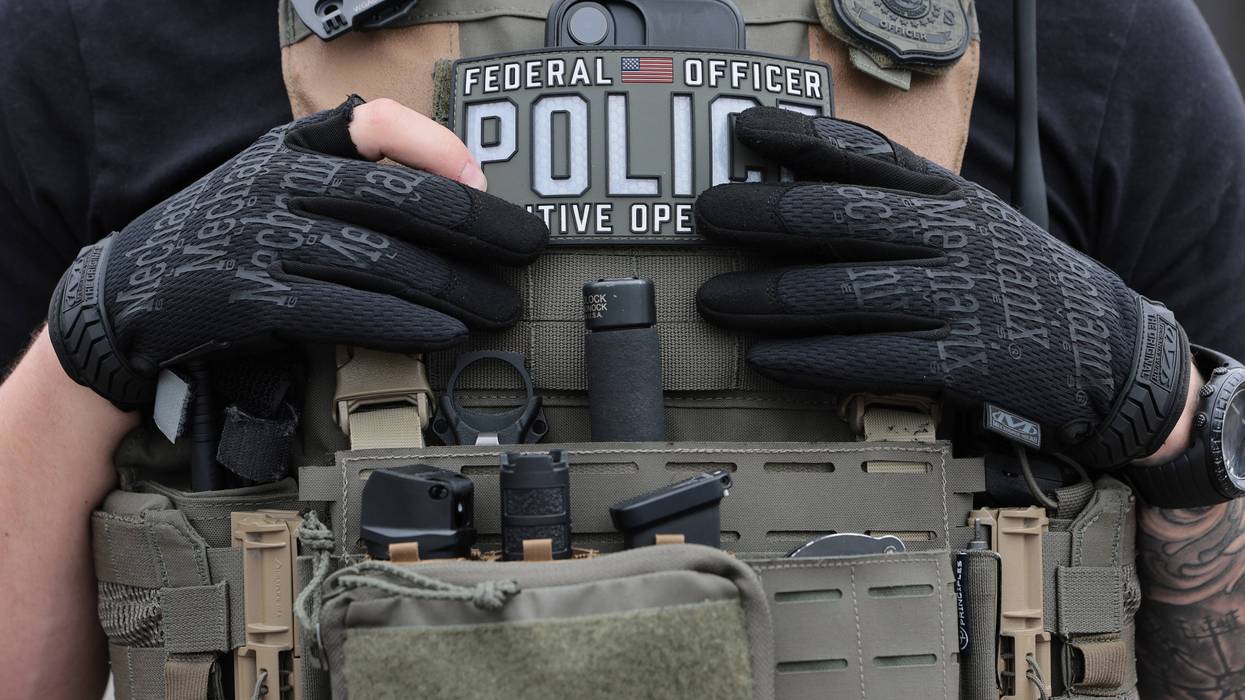 Federal officer in tactical vest, black gloves, with 'POLICE' and 'ICE' patches.