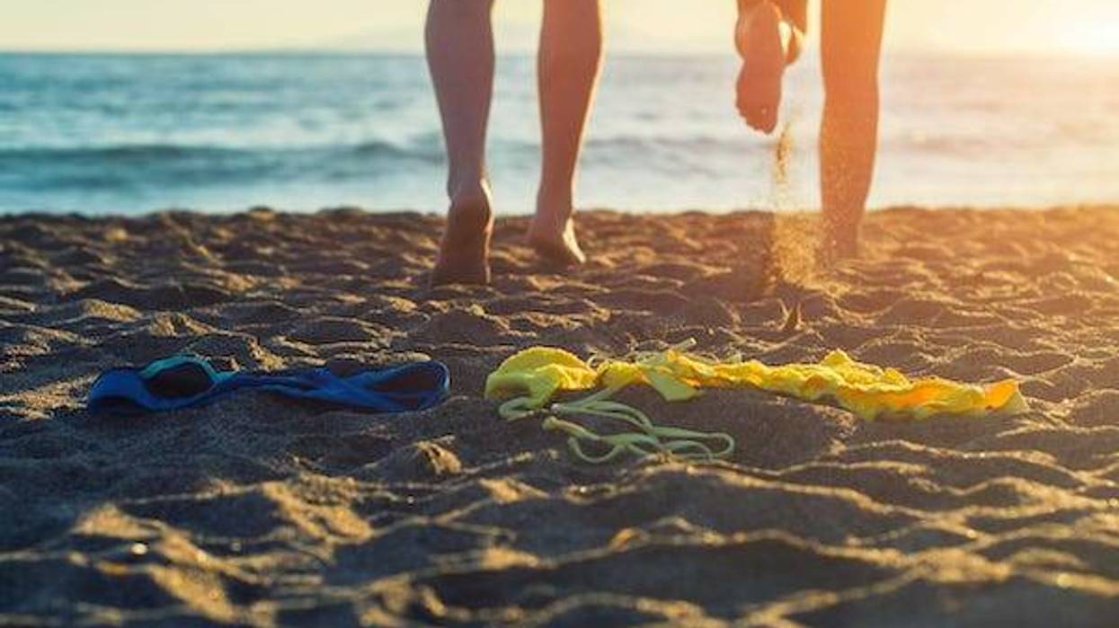Female and male legs with bikini and swimming trunks on the sand on a sunset background