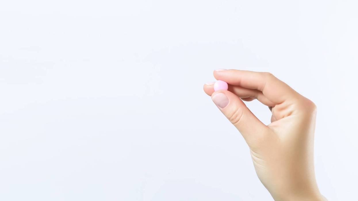 female hand holds a round pink pill on a blue background
