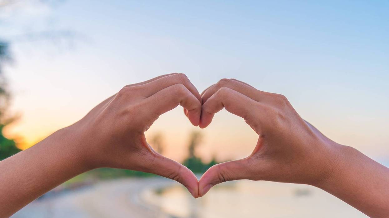Female hands in the form of heart against sunlight in sunset sky, twilight time