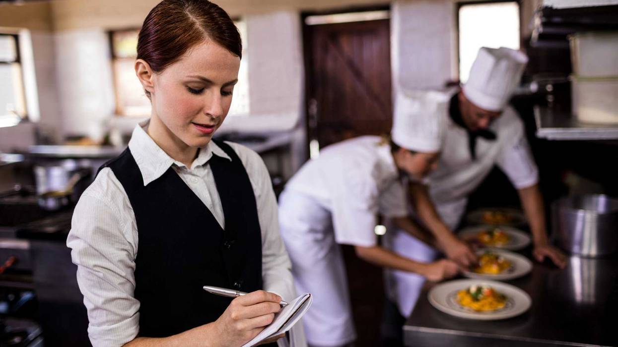 Female waitress noting an order on notepad in kitchen at hotel