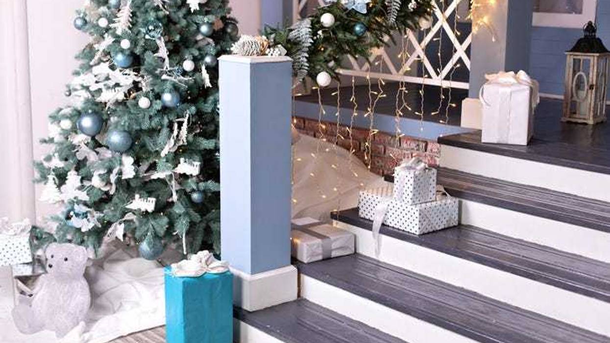 Festive outdoor design home with Xmas tree and gifts in yard. House entrance staircase decorated for winters holidays, gifts, branches fir and glowing garland. Cozy wooden porch of the house with gift