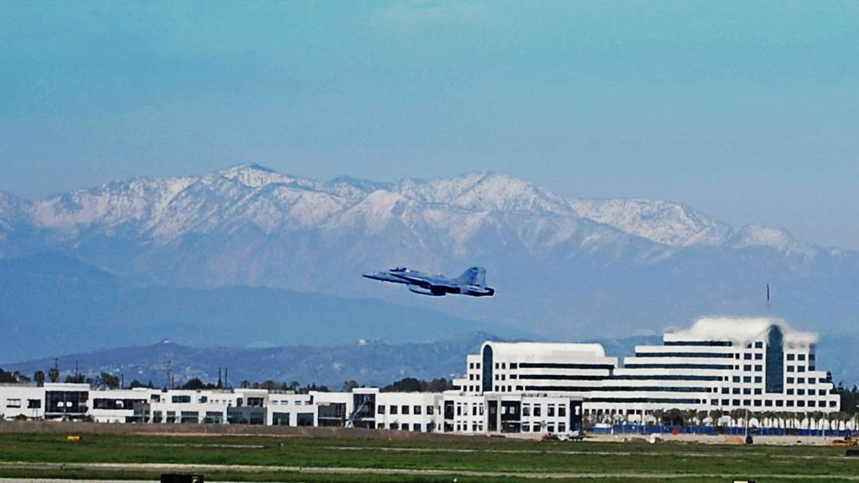 Fighter jet taking off from Long Beach Airport in Long Beach, CA. Snow covered mountains in the background.