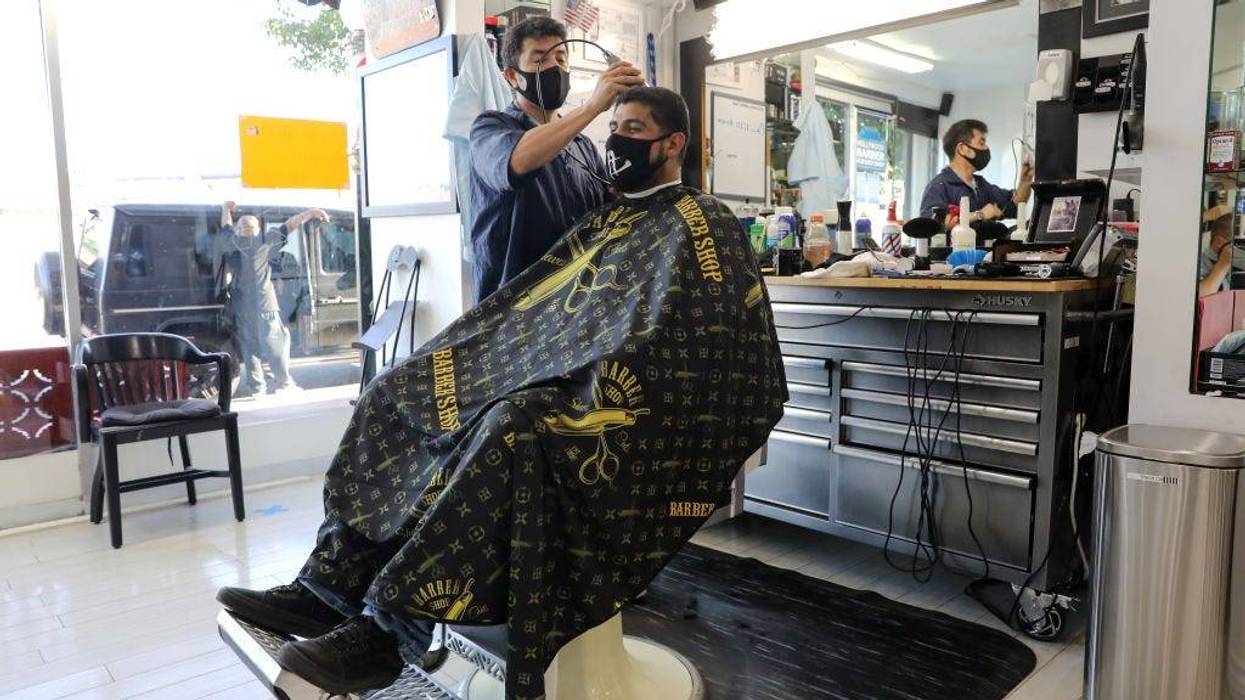 FILE - A barber and his client wear face masks in the Hollywood Barber Shop shortly before closing amid new restrictions due to the COVID-19 pandemic on July 13, 2020 in Los Angeles.