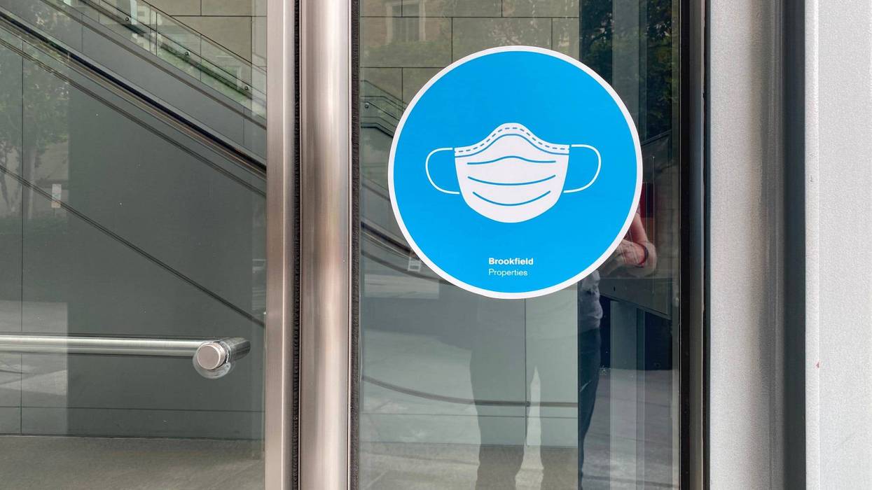 FILE - Blue window sign with a white mask at office entrance indicates face coverings required during Covid-19 viral pandemic in Downtown Los Angeles.