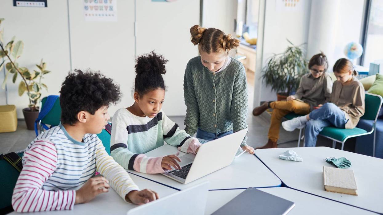 File - High angle view of a group of children working together at desk in classroom.