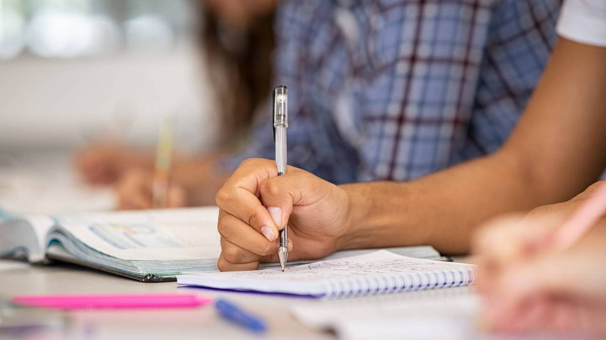 File image - Close up of a student's hand on the table in a classroom taking notes. Two students at a charter school in Temecula were recently forced off the campus after refusing to wear a mask due to religious reasons.