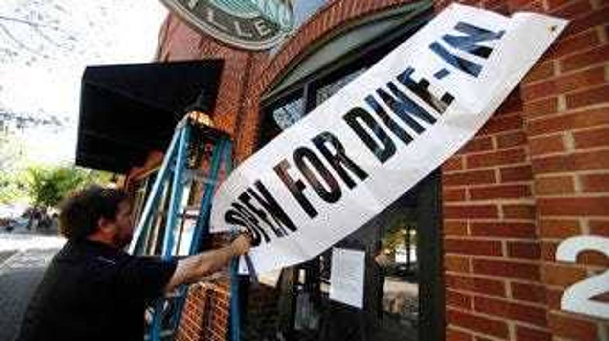 FILE - In this April 27, 2020, file photo, Jason Godbey hangs a banner over the entrance of Madison Chop House Grille as they prepare to shift from take out only to dine-in service in Madison, Ga. (AP Photo/John Bazemore, File)