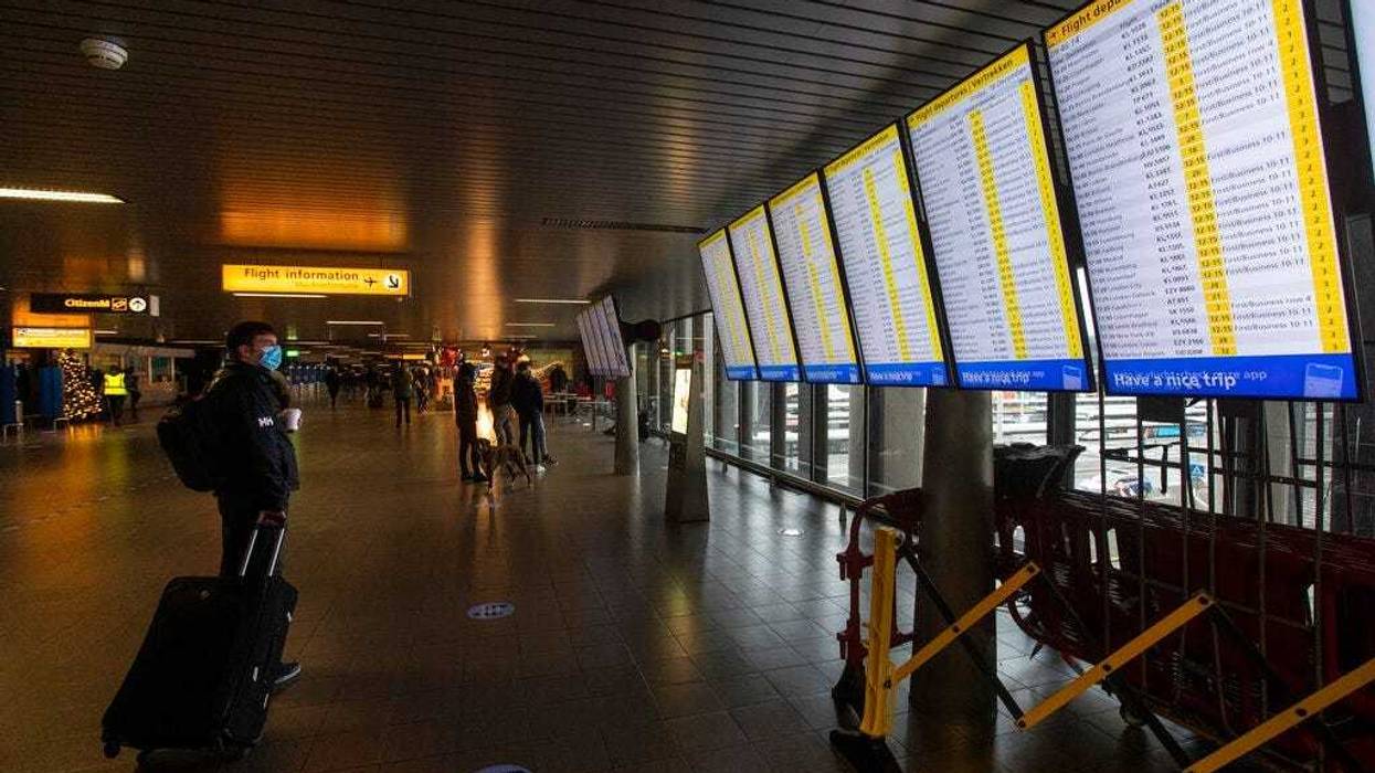 FILE- In this Friday Dec. 18, 2020, file photo, A traveller wearing a face mask checks the flight departures at Schiphol Airport, near Amsterdam, Netherlands.