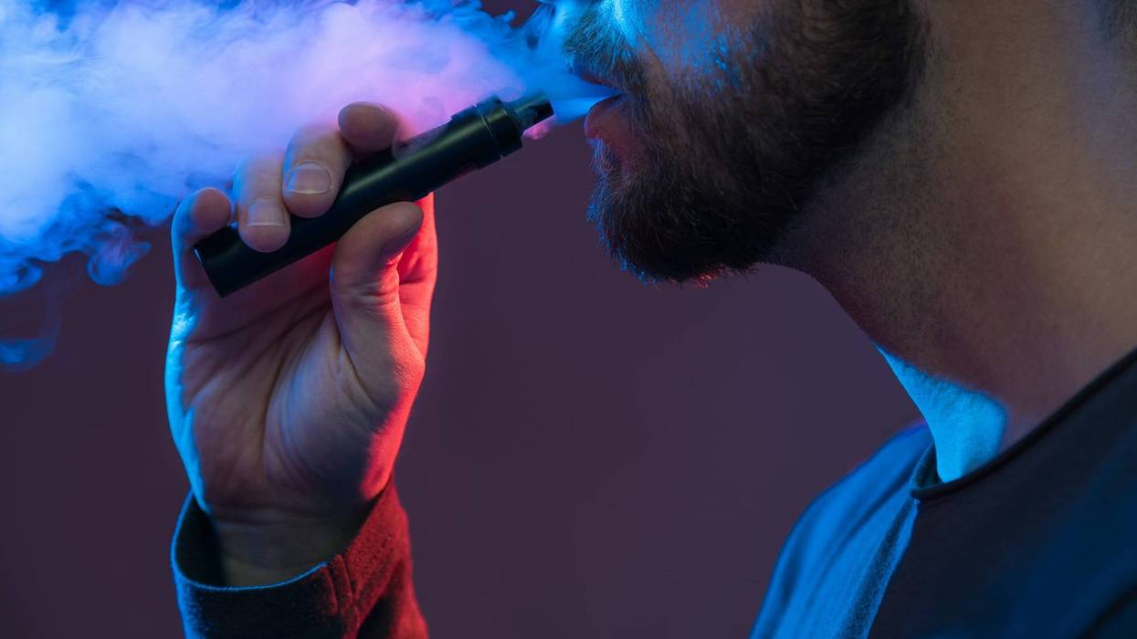 File photo of a man smoking an e-cigarette against a purple background.